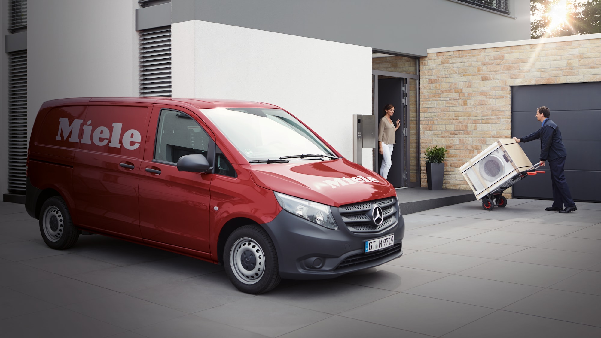 a Miele delivery person with a Miele delivery van bringing a Miele washing machine to a womans at her door