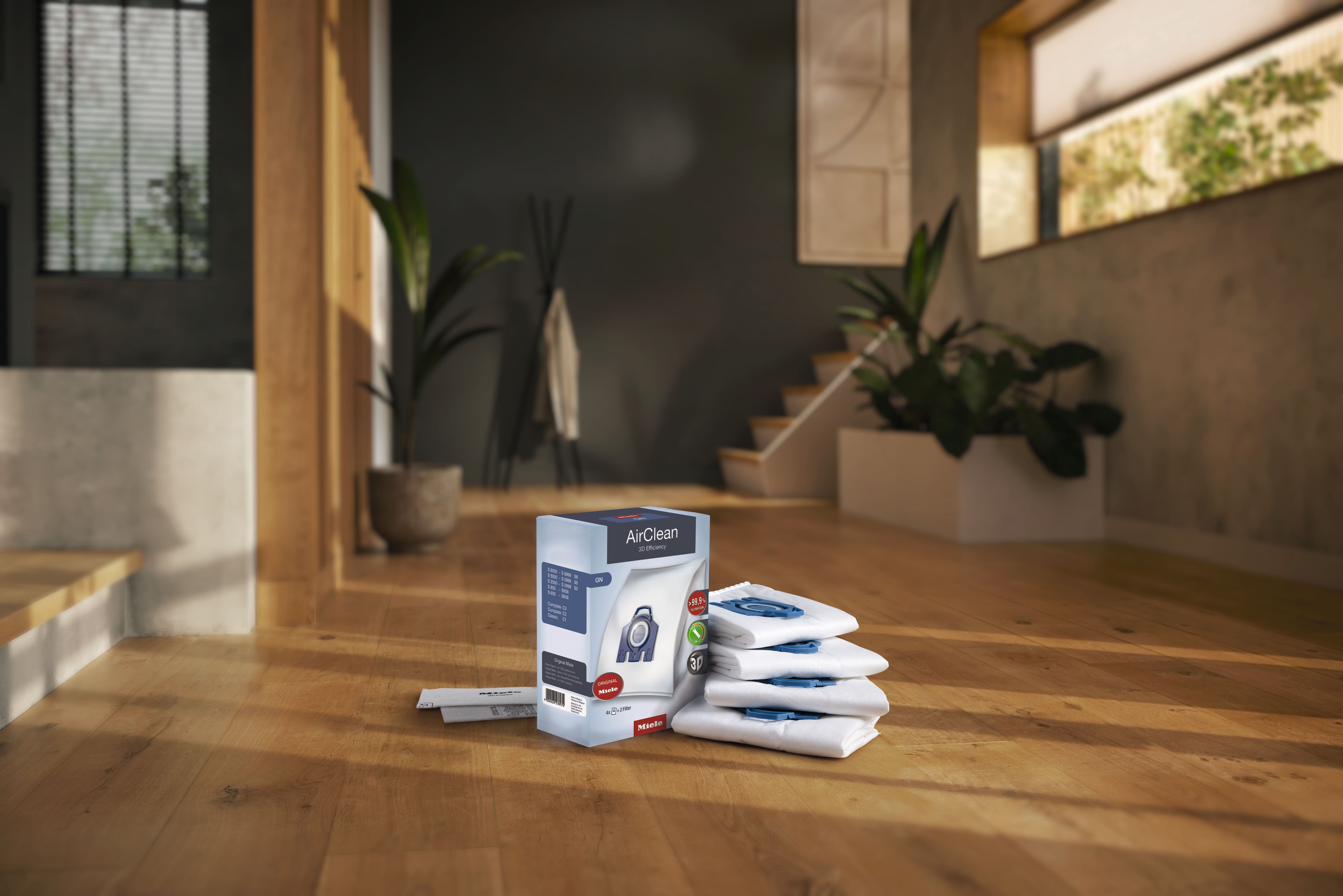 Box of vacuum bags, with 4 bags and two exhaust filters sitting on the wood floor inside a house